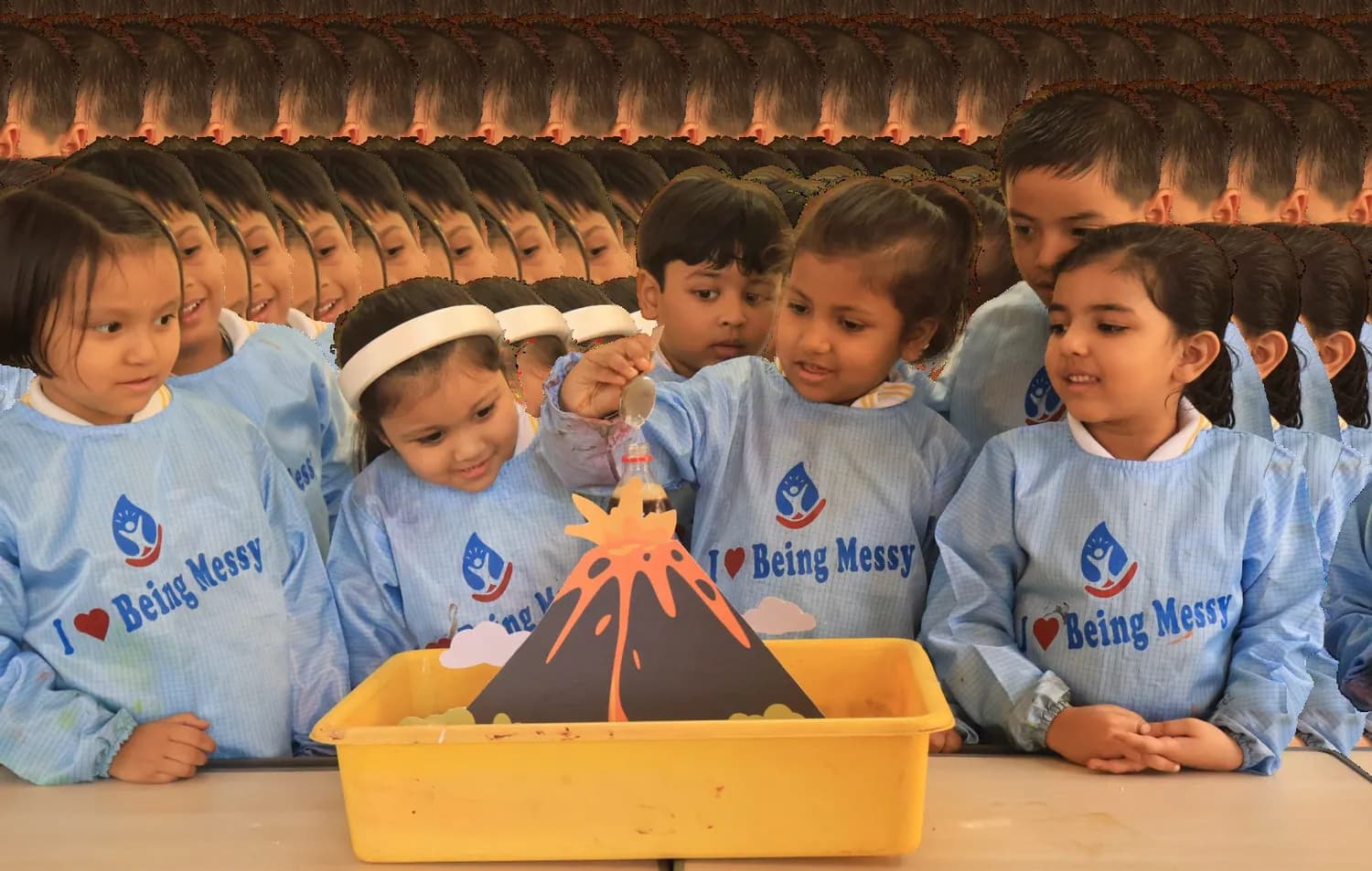 Children in aprons watching a model volcano erupt