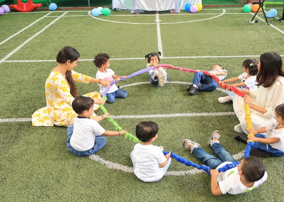 Children and teachers seated in a circle holding a ribbon on the school field