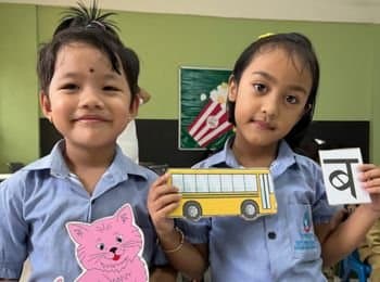 Two Boond children holding up a paper bus and a Hindi letter card